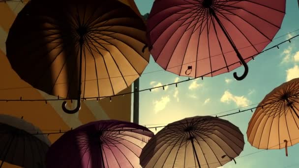 Pouliční dekorace s pestrobarevnými deštníky, na slunci, proti modré obloze — Stock video