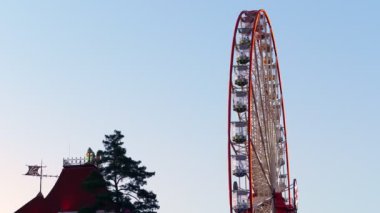 Yan görünüş. Gökyüzüne, günbatımına, alacakaranlığa karşı aydınlatmalı geniş dönme dolap..