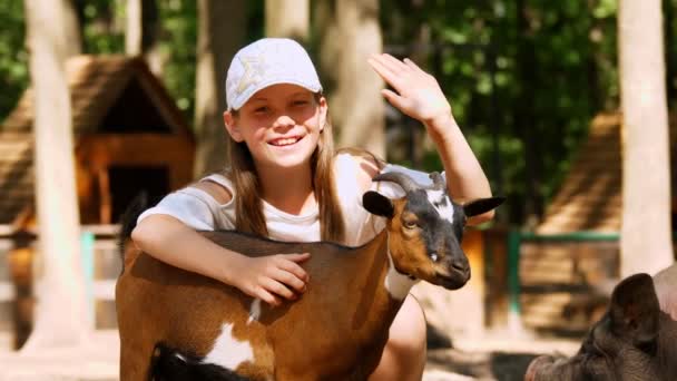 Kind, meisje strelen een kleine geit kind, in een kinderboerderij of op een boerderij. staat tussen verschillende geiten en biggetjes. het meisje is erg gelukkig. — Stockvideo