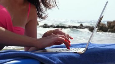 Yakın plan, parlak turuncu tırnaklı kadın elleri dizüstü bilgisayarda, deniz kenarında, sıcak yaz gününde bir şeyler yazıyor. Serbest çalışan, uzaktan kumandalı. Denizde yaz tatili
