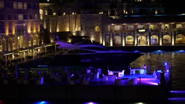 Colorida iluminación nocturna de la ciudad. una hermosa vista de la terraza abierta en el paseo marítimo, en el puerto deportivo con yates estacionados. programa de entretenimiento nocturno. noche de verano — Vídeo de stock