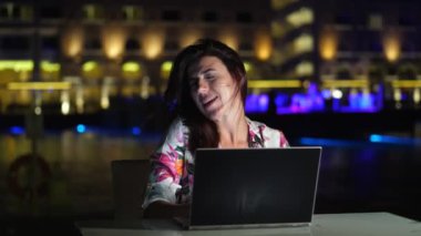 Güzel genç bir kadın dizüstü bilgisayar kullanır ve müzik dinler, şarkı söyler, zevkle dans eder. Açık terasta ya da balkonda oturuyor. Gece şehrin parlak ışıklarının arka planında. Sıcak yaz gecesi.