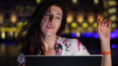 Güzel genç bir kadın dizüstü bilgisayar kullanır ve müzik dinler, şarkı söyler, zevkle dans eder. Açık terasta ya da balkonda oturuyor. Gece şehrin parlak ışıklarının arka planında. Sıcak yaz gecesi.