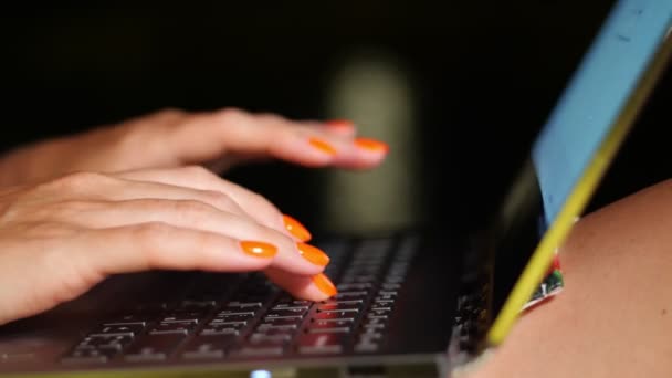 Zbliżenie, kobiece ręce z jasnoczerwonymi paznokciami, wpisują na klawiaturze laptopa, na rozmytym tle świateł nocnych miasta. — Wideo stockowe
