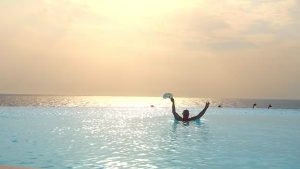 Hombre divirtiéndose en la piscina infinita al aire libre con vistas panorámicas al mar, al amanecer. concepto de viaje y vacaciones — Vídeo de stock