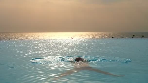 男は日の出にパノラマの海の景色を望む屋外インフィニティプールで泳ぐ。旅行や休暇のコンセプト — ストック動画