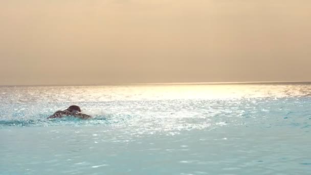 O homem nada habilmente, com um golpe, trabalha a técnica na piscina infinita exterior com vista panorâmica do mar, ao nascer do sol. esporte, viagens e férias conceito — Vídeo de Stock