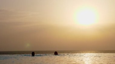 Siluetler, kadın ve genç kız, anne ve kız güneş doğarken panoramik deniz manzaralı açık havada sonsuzluk havuzunda yüzerler. Aile tatili kavramı