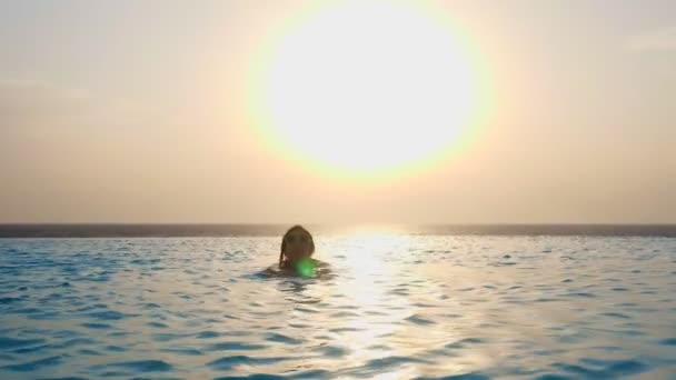 Sylwetka, kobieta, w okularach przeciwsłonecznych, pływa w odkrytym basenie infinity z panoramicznym widokiem na morze, o wschodzie słońca. koncepcja podróży i wakacji — Wideo stockowe