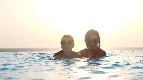 Mulher e adolescente menina, mãe e filha, em engraçado, idêntico, óculos de sol redondos, relaxar, se divertir na piscina ao ar livre com vista panorâmica do mar, ao nascer do sol. conceito de férias em família . — Vídeo de Stock