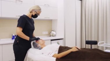 Kozmetik bilimci, maske ve eldiven takarak, özel ıslak mendilli kadın yüzünden kozmetik yüz ürününün kalıntılarını çıkarıyor. Kozmetik kliniğinde veya güzellik salonunda cilt bakımı prosedürü.