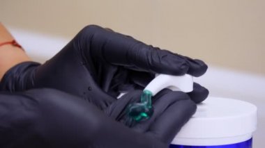 Yakın plan, siyah tıbbi eldivenli eller kozmetik ürünü sıkar, şeker kutusundan yeşil jel çıkarır. Tıp, kozmetoloji. Antiseptik maddeler..