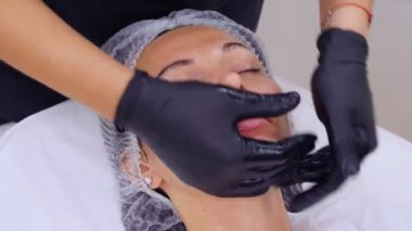 Siyah tıbbi eldivenlerle kozmetik uzmanı, kozmetik kliniğinde ya da güzellik salonunda özel kozmetik jel kullanan bir kadına cilt bakımı, yüz masajı yapıyor..