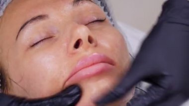 Siyah tıbbi eldivenlerle kozmetik uzmanı, kozmetik kliniğinde ya da güzellik salonunda özel kozmetik jel kullanan bir kadına cilt bakımı, yüz masajı yapıyor..