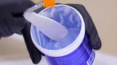 Yakın plan, siyah eldivenli kozmetik uzmanı, özel spatula ya da kaşıkla maske takmak için mavi kozmetik ürünü seçiyor. Kozmetik kliniğinde veya güzellik salonunda cilt bakımı prosedürü.