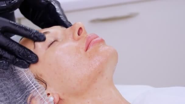 Close-up, cosmetoloog, in zwarte medische handschoenen, voert huidverzorging procedure, gezichtsmassage aan een vrouw, met behulp van speciale cosmetische gel, in cosmetische kliniek of schoonheidssalon. — Stockvideo