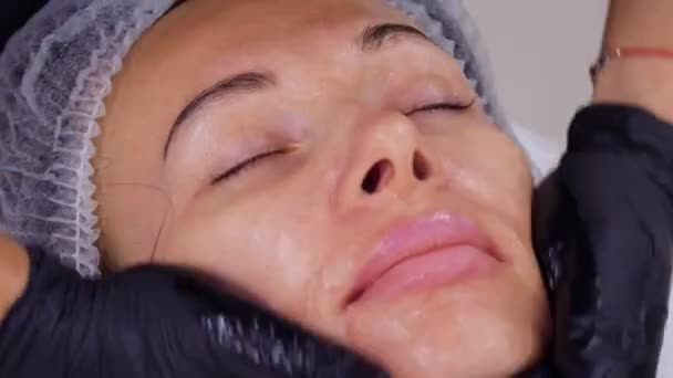 Nahaufnahme, Kosmetiker, in schwarzen medizinischen Handschuhen, führt Hautpflege durch, Gesichtsmassage für eine Frau, mit speziellem kosmetischen Gel, in der Kosmetikklinik oder im Schönheitssalon. — Stockvideo