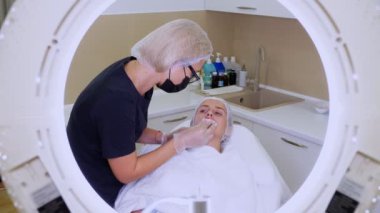Dudak büyütme prosedürü. Cerrah, tıbbi eldiven ve maske takıyor, yoğurma yapıyor, dudaklara hyaluronik asit dağıtmak için dudaklara masaj yapıyor. Güzellik iğneleri. Estetik ameliyat.