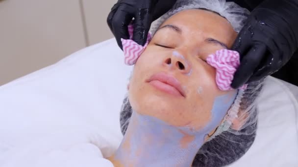 Primo piano, il cosmetico, in guanti medici neri, toglie resti di maschera di faccia cosmetica, da faccia femminile con salviettine umide speciali. procedura di cura della pelle in clinica cosmetologica o salone di bellezza. — Video Stock