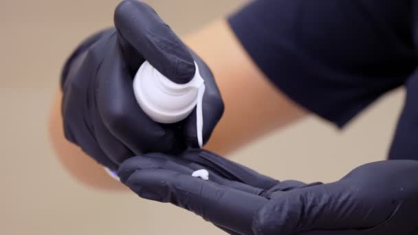 Close-up, τα χέρια σε μαύρα ιατρικά γάντια αποσπάσει λευκή καλλυντική κρέμα από ένα διανομέα. έννοια φροντίδας του δέρματος. Αισθητική, κομμωτήριο. φάρμακο. — Αρχείο Βίντεο