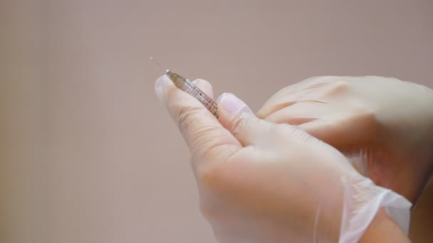 Close-up, a hand in a white medical glove holds a small syringe with hyaluronic acid or possibly another liquid. beauty injections, lip augmentation procedure. — Stock Video