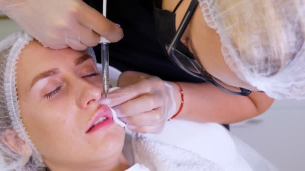 Kvinnan får en skönhetsinjektion på läpparna. Kirurg, i medicinska handskar, genomborrar överläppen med spruta och injicerar långsamt hyaluronsyra. Läppförstoringsförfarande. Plastkirurgi. — Stockvideo