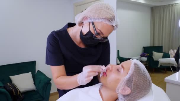 Läppförstoringsförfarande. Kirurg, i medicinsk mask och handskar, knådar och masserar kvinnliga läppar för att jämnt fördela hyaluronsyra i dem efter skönhetsinjektioner. Plastkirurgi. — Stockvideo