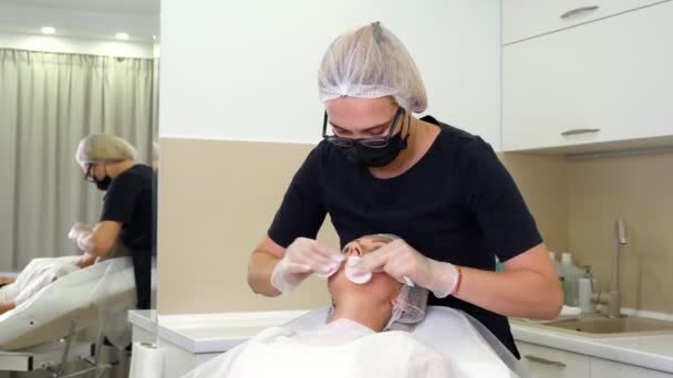 Женщина врач, в медицинских перчатках и маске, вытирает женские губы антисептическим и анестезирующим раствором хлопка колодки, перед процедурой увеличения губ с помощью гиалуроновой кислоты инъекции. — стоковое видео