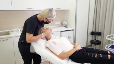 Dudak büyütme prosedürü. Cerrah, tıbbi maske ve eldivenlerle kadın dudaklarına masaj yaparak güzellik iğnelerinden sonra hyaluronik asit dağıtıyor. Estetik ameliyat.