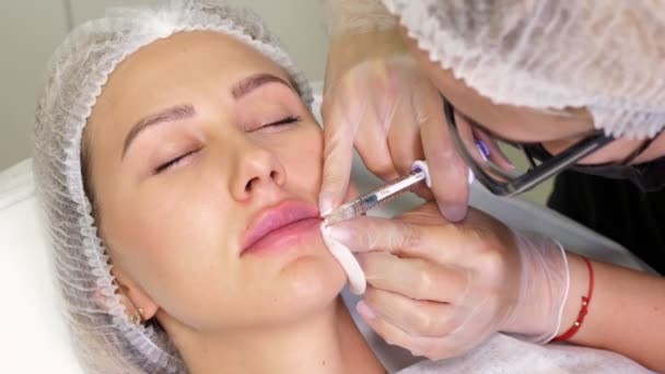 Close-up, female face. Surgeon, in medical gloves, carefully and slowly injects hyaluronic acid into womans lips with a syringe. lip augmentation procedure. beauty injections. Plastic surgery. — Stock Video