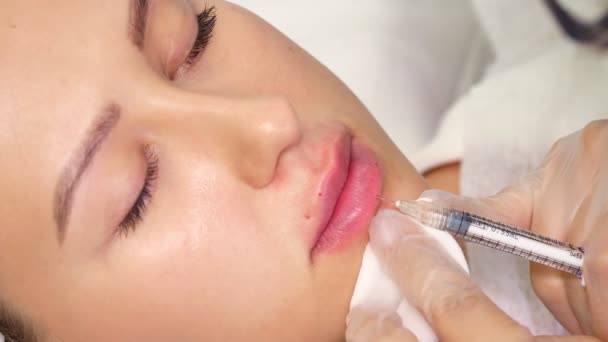 Close-up, female face. Surgeon, in medical gloves, carefully and slowly injects hyaluronic acid into womans lips with a syringe. lip augmentation procedure. beauty injections. Plastic surgery. — Stock Video