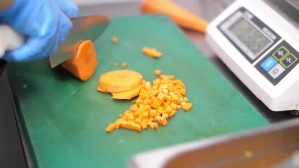 Close-up, the chef, in protective gloves, is cutting carrot on a cutting board. cooking, food, canteen, catering. health, safety and reopening concept — Stock Video