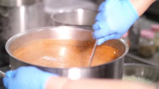 Close-up. Chef usando luvas de proteção está mexendo sopa de tomate ou borscht com colher grande em panela grande. alimento saudável, cozinhar, conceito de segurança. cantina de reabertura — Vídeo de Stock