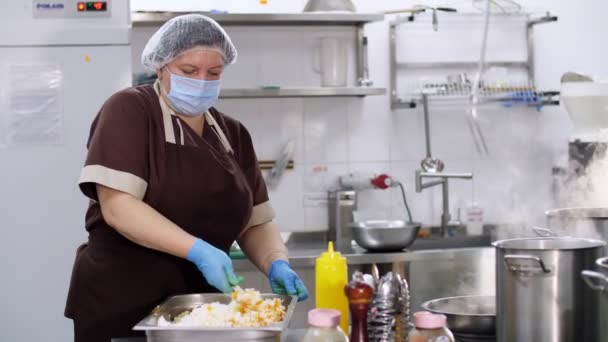 Cucino. donna chef, in guanti protettivi e una maschera, prepara il cibo in cucina, in mensa. concetto di salute, alimentazione e sicurezza. mensa di riapertura — Video Stock