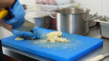 Yemek pişirmek. Yakın plan, koruyucu eldivenli şef, pişirme tahtasındaki haşlanmış patatesleri kesiyor. Sağlıklı gıda ve güvenlik kavramı. Matarayı yeniden aç