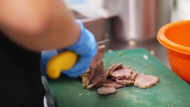 Yemek pişirmek. Yakın plan, koruyucu eldivenli şef et kesiyor, pişirme tahtasında haşlanmış domuz eti var. Sağlıklı gıda ve güvenlik kavramı. Matarayı yeniden aç