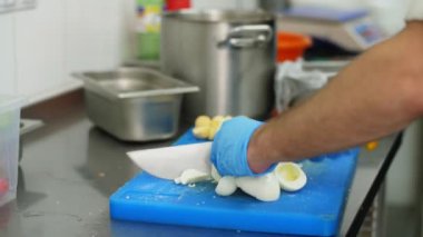Yemek pişirmek. Yakın plan, koruyucu eldivenli şef, pişirme tahtasında haşlanmış yumurta kesiyor. Sağlıklı gıda ve güvenlik kavramı. Matarayı yeniden aç