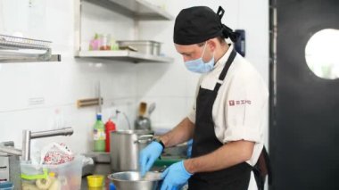 Yemek pişirmek. Aşçı adam koruyucu eldivenler ve maske takıyor. Mutfakta, kantinde yemek hazırlıyor. Sağlıklı gıda ve güvenlik kavramı. Matarayı yeniden açıyorum. Gönüllülük ve yardım