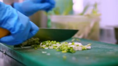 Yemek pişirmek. Yakın plan, koruyucu eldivenli şef, yemek tahtasında yeşil soğan kesiyor. Sağlıklı yemek. Güvenlik kavramı. Matarayı yeniden açıyorum. Gönüllülük ve yardım