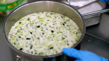 Yemek pişirmek. Yakın plan. Şef, koruyucu eldivenler içinde, tuzu ve tencerede çorbayı büyük kaşıkla karıştırıyor. Sağlıklı yemek. Güvenlik kavramı. Matarayı yeniden açıyorum. Gönüllülük ve yardım