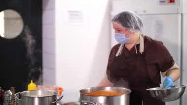 Yemek pişirmek. Kadın şef, koruyucu eldiven ve maske takıyor, mutfakta yemek hazırlıyor, kantinde. Sağlıklı yemek. Güvenlik kavramı. Matarayı yeniden açıyorum. Gönüllülük ve yardım