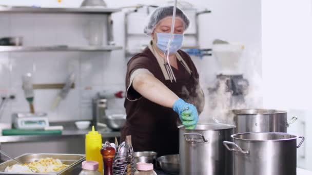 Kochen. Die Köchin bereitet in Schutzhandschuhen und Maske in der Küche, in der Kantine, das Essen zu. Gesundheits- und Sicherheitskonzept. Wiedereröffnung der Kantine — Stockvideo