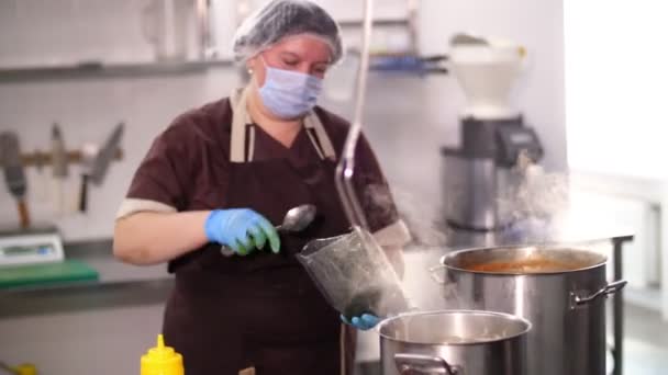 Cooking. woman chef, in protective gloves and mask, prepares food in the kitchen, in canteen. health food. safety concept. reopening canteen. volunteering and charity — Stock Video