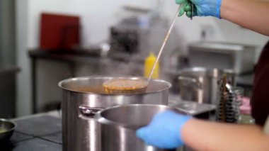 Yemek pişirmek. Yakın plan. Şef koruyucu eldivenlerle büyük bir tencereden küçük bir kaba sıcak portakal çorbası döker. Sağlıklı yemek. Gönüllü olmak ve yardım. Matarayı yeniden açıyorum. güvenlik kavramı.