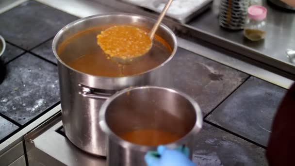 Koken. close-up. de chef-kok, in beschermende handschoenen, giet hete sinaasappelsoep van een grote pan in een kleinere container. Gezondheidsvoedsel. vrijwilligerswerk en liefdadigheid. Kantine heropenen. veiligheidsconcept. — Stockvideo
