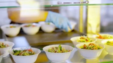 Yemek pişirmek. Yakın plan. Garson, koruyucu eldivenlerle, salata kaselerini self-servis yemek vitrinine koyuyor. Mutfak kafeteryasında açık büfe yemek. Sağlıklı yemek. Gönüllü olmak ve yardım. yeniden açılıyor