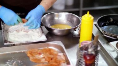 Yemek pişirmek. Yakın plan. Şef, koruyucu eldivenlerle, un içinde çiğ tavuk pirzolası ve çırpılmış çiğ yumurta pişirir, sonra da tavada pişirir. Sağlıklı yemek. Gönüllü olmak ve yardım. Yeniden açılıyor. güvenlik kavramı.