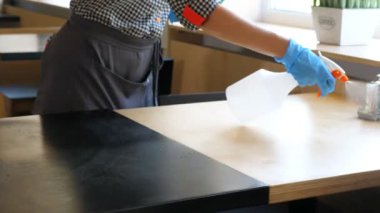 Yakın plan. Garson, koruyucu eldiven giyiyor, ziyaretçiler için masaları dezenfekte ediyor. Koronavirüsü korumak için antiseptik sprey kullanıyor. Kafeteryayı ya da restoranı yeniden açmak. güvenlik kavramı.