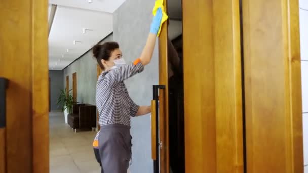 Kvinnlig städerska, i skyddsmask och handskar, torkar dörrhandtag med antiseptiskt medel i restaurang eller offentlig inrättning. skydd mot coronavirus, säkerhetskoncept — Stockvideo
