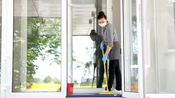 Donna donna delle pulizie, in maschera protettiva e guanti, pulisce tappeto speciale con una soluzione antisettica all'ingresso del ristorante o istituzione pubblica. protezione contro covid-19, concetto di sicurezza — Video Stock